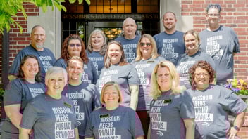 15 members of the MSTA Board pose outside the MSTA headquarters in shirts that say "Missouri Needs Public Schools."