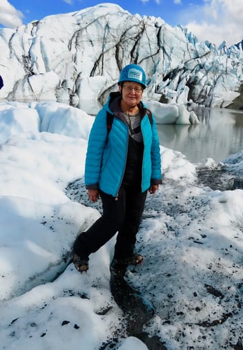 A woman in a blue coat and hard hat stands in an icy landscape