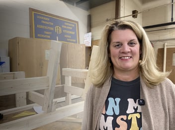 Amy Kelsey stands in a shop classroom beside an unfinished wooden bench and an FFA sign
