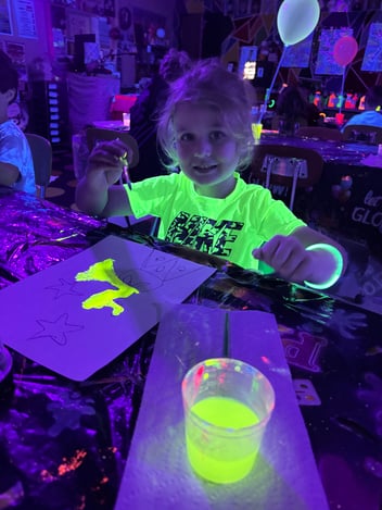 A young girl wears a neon shirt and paints with neon paints