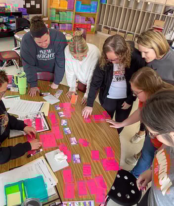 Teachers work together on an activity at a table with pink sticky notes