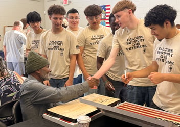 An elderly man shakes hands with a high school student