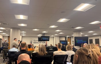 A room full of people sit in a meeting