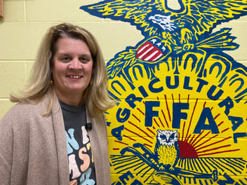 MSTA President Amy Kelsey stands next to a yellow FFA logo painted on a wall