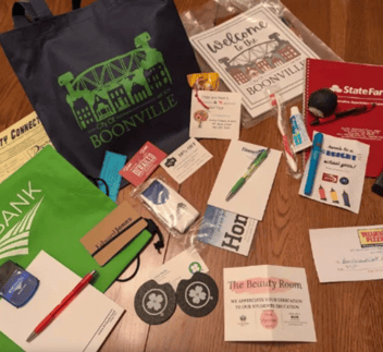 Items are scattered on a table to be put in a welcome bag including coasters, notebooks, pens, a toothbrush, and coupons.