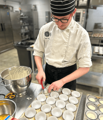 A high school boy works in a large kitchen and fills a muffin tin with melted white chocolate