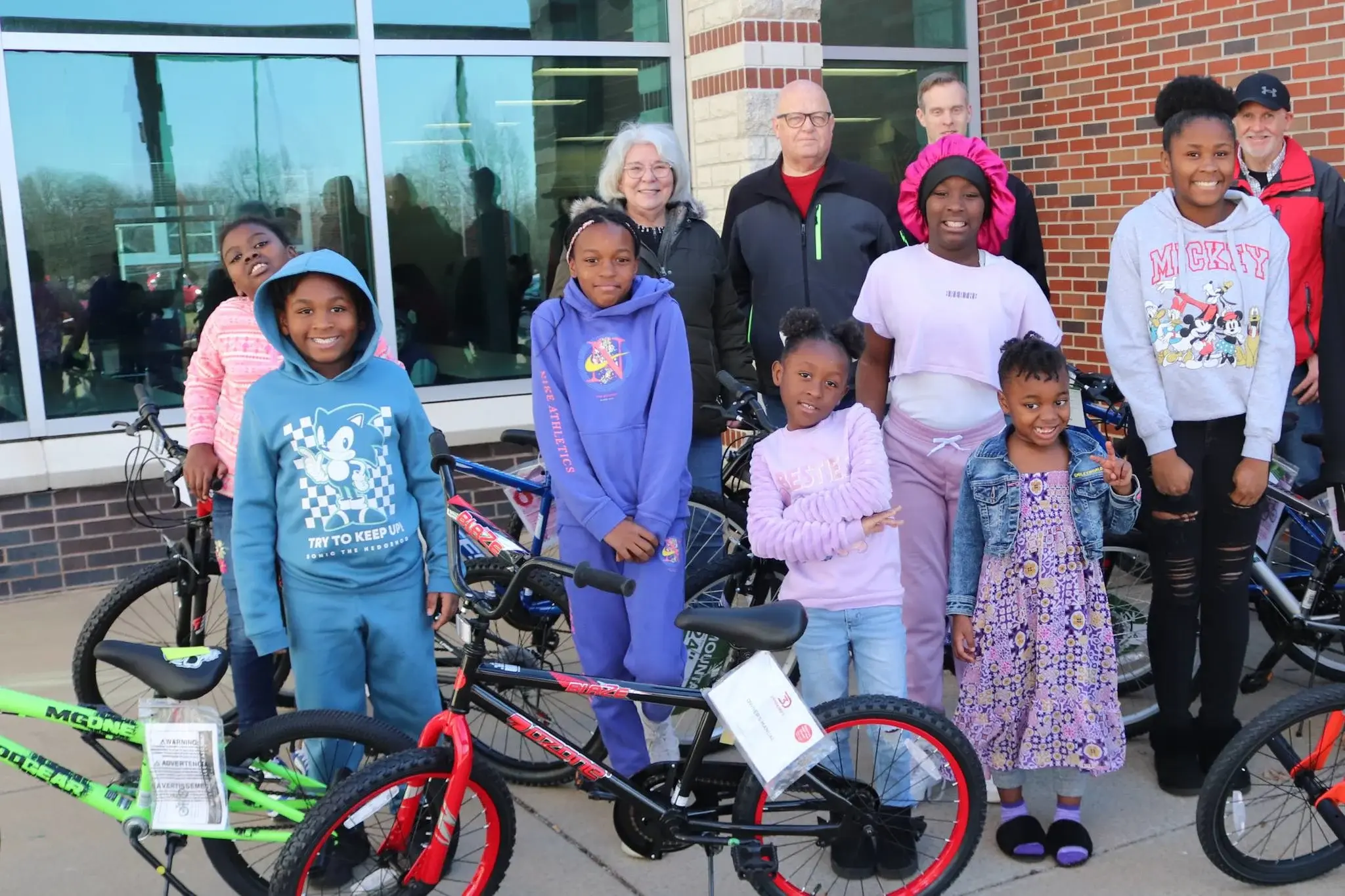 Students ranging in age stand smiling next to new bikes.