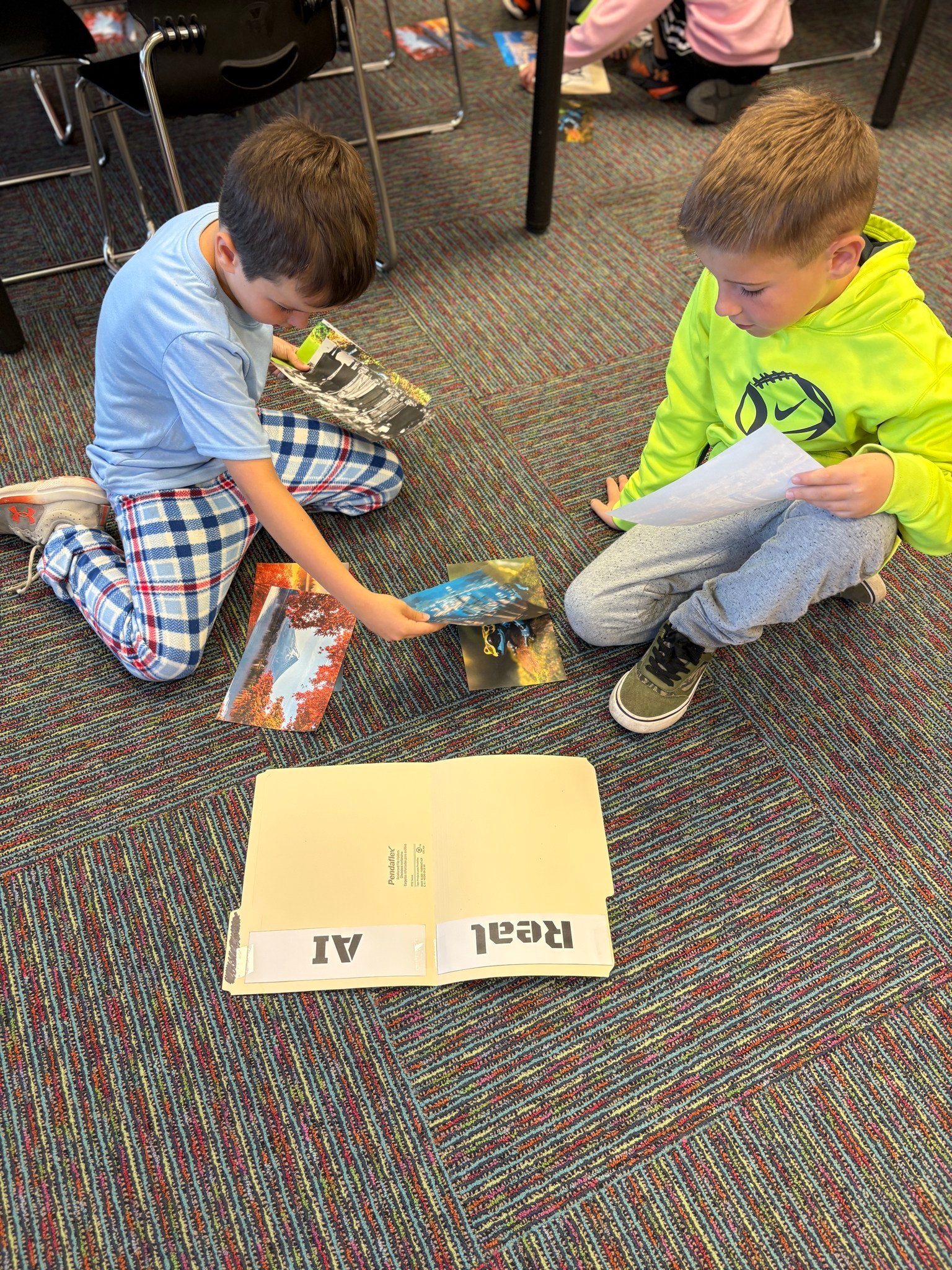 Two elementary-aged boys look at photos beside a folder that reads "Real" and "AI"