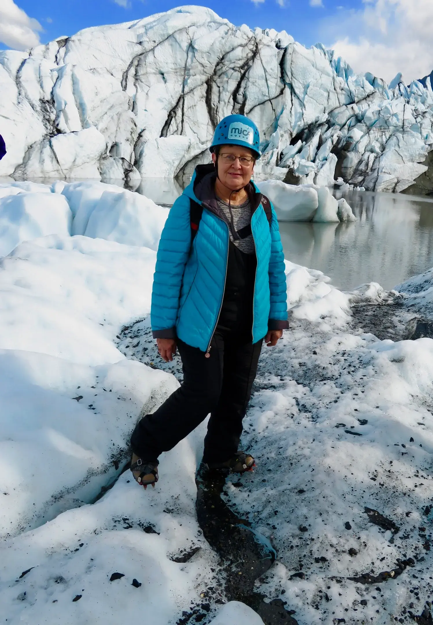 A woman in a blue coat and hard hat stands in an icy landscape