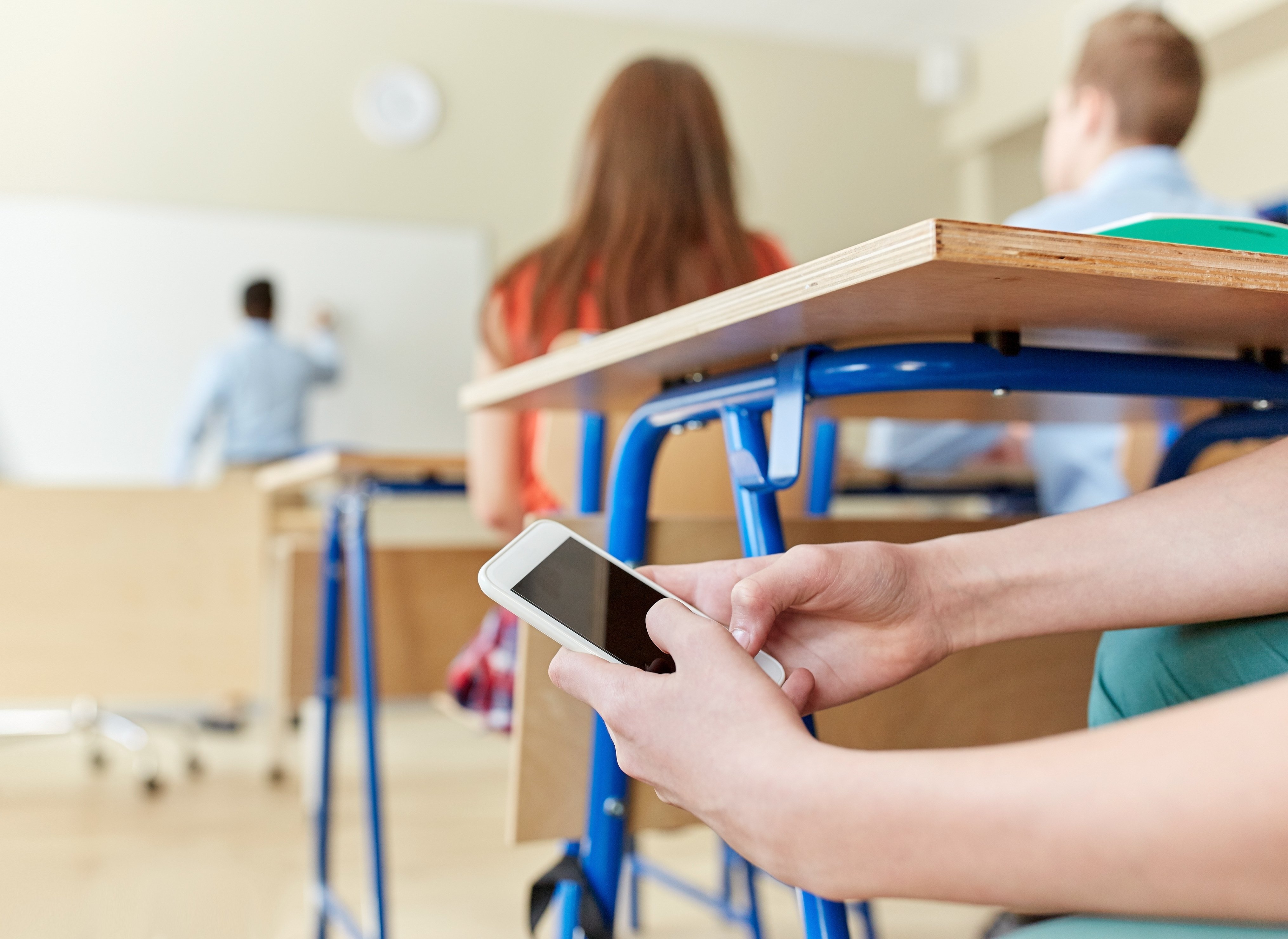 A student uses a cell phone under a desk