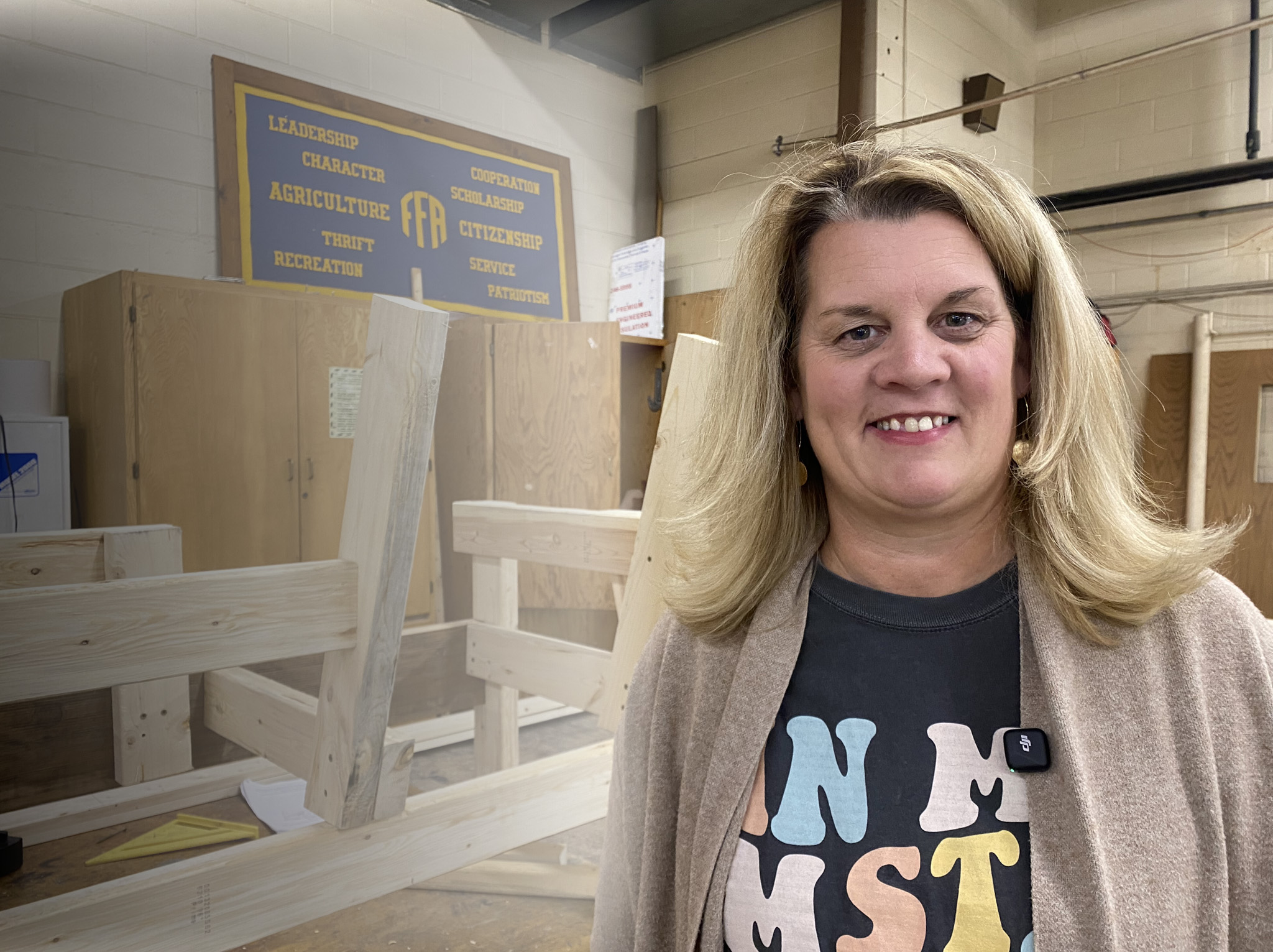 Amy Kelsey stands in a shop classroom beside an unfinished wooden bench and an FFA sign