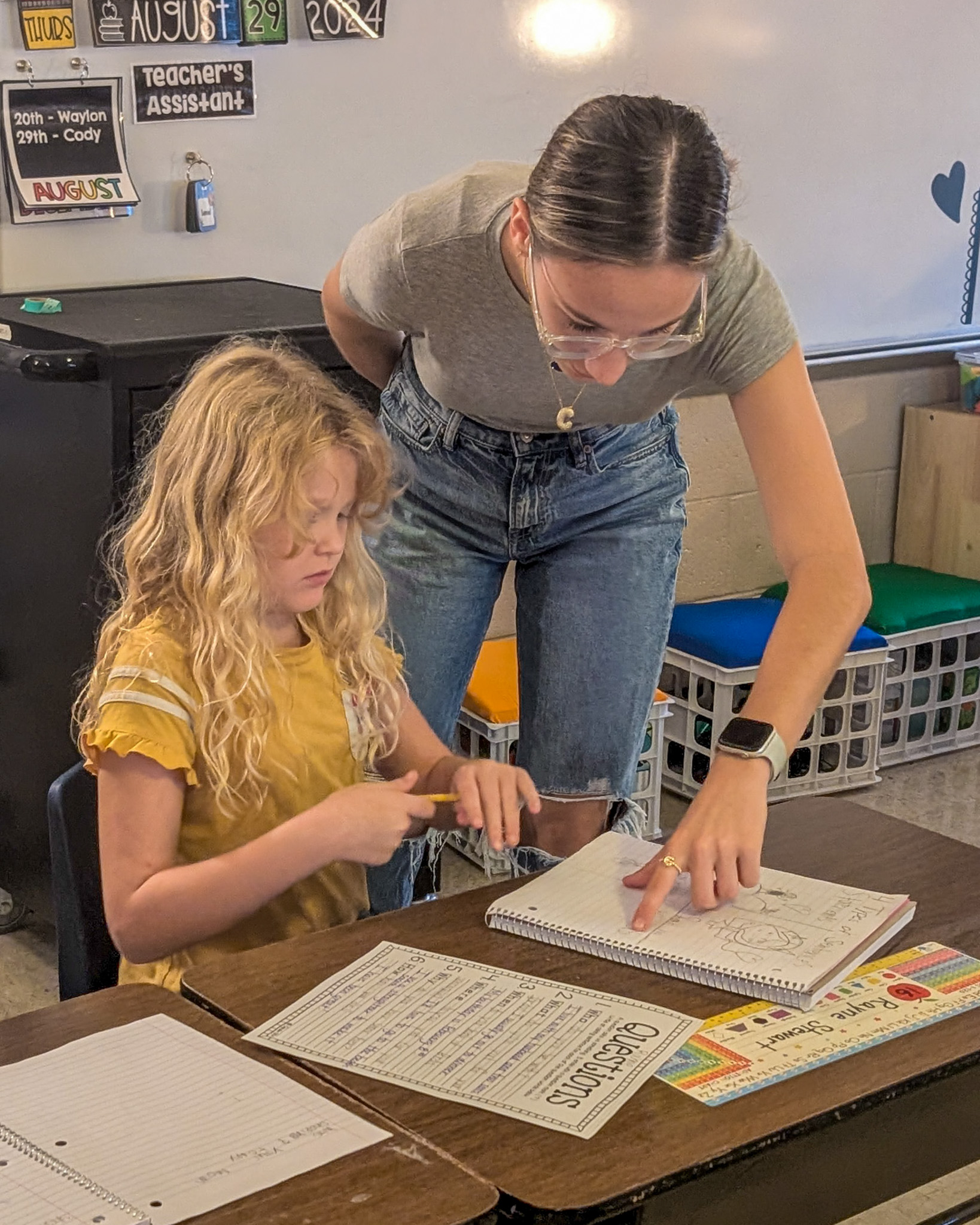 A high school student points to a notebook in front of an elementary student