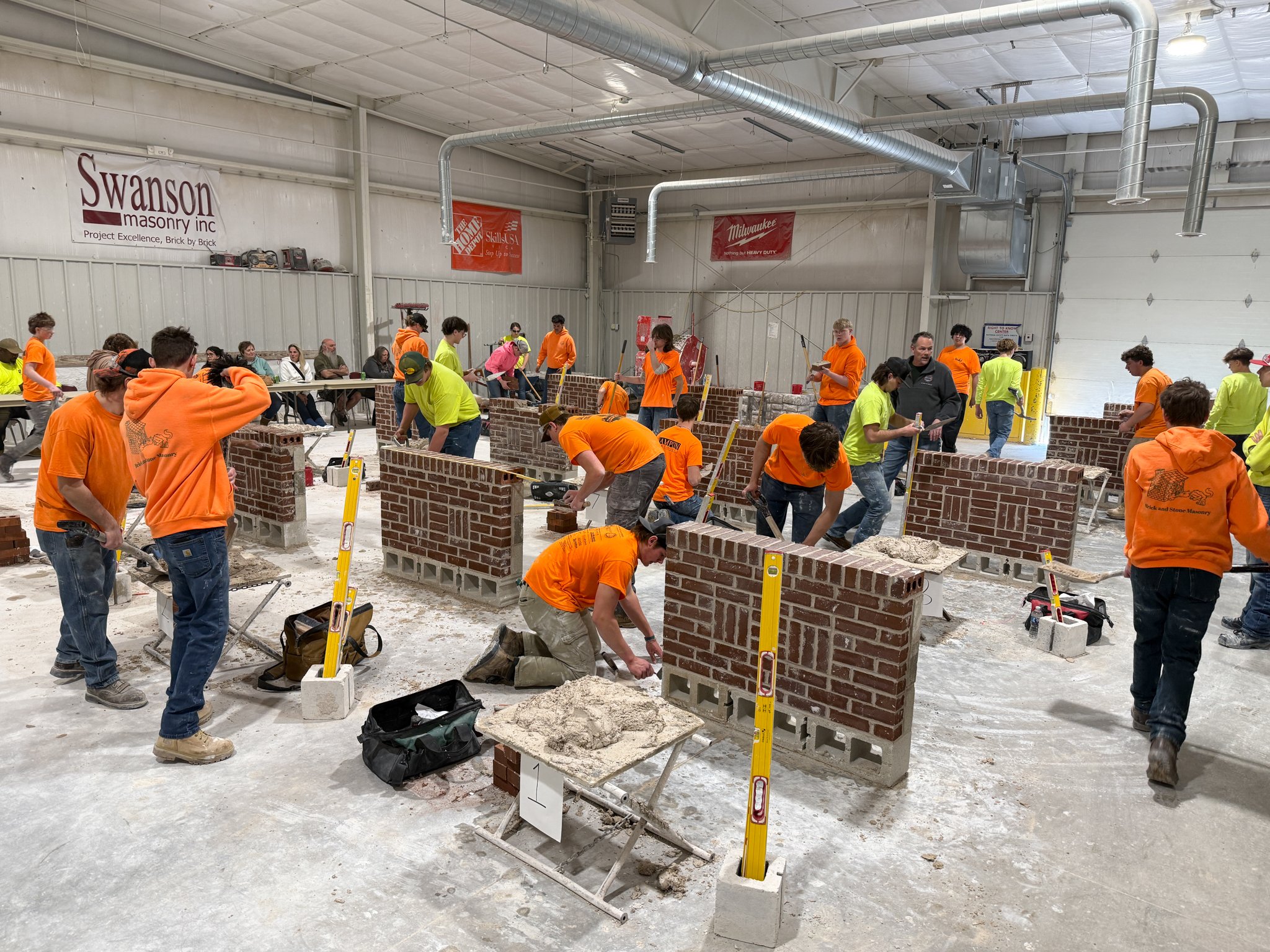 High school students build small brick walls in a shop room