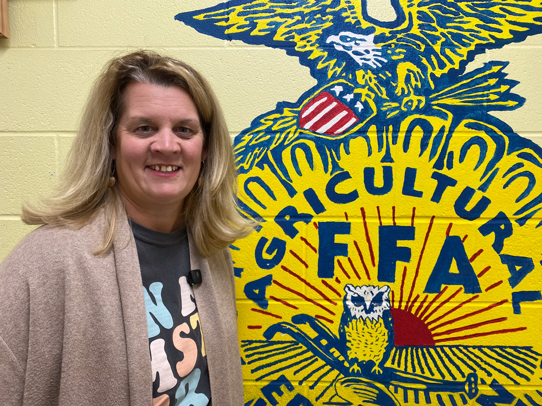 MSTA President Amy Kelsey stands next to a yellow FFA logo painted on a wall