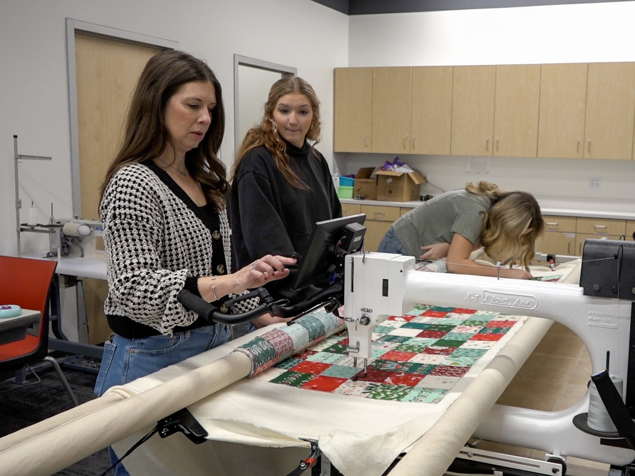 A teenage girl supervises a longarm quilting machine