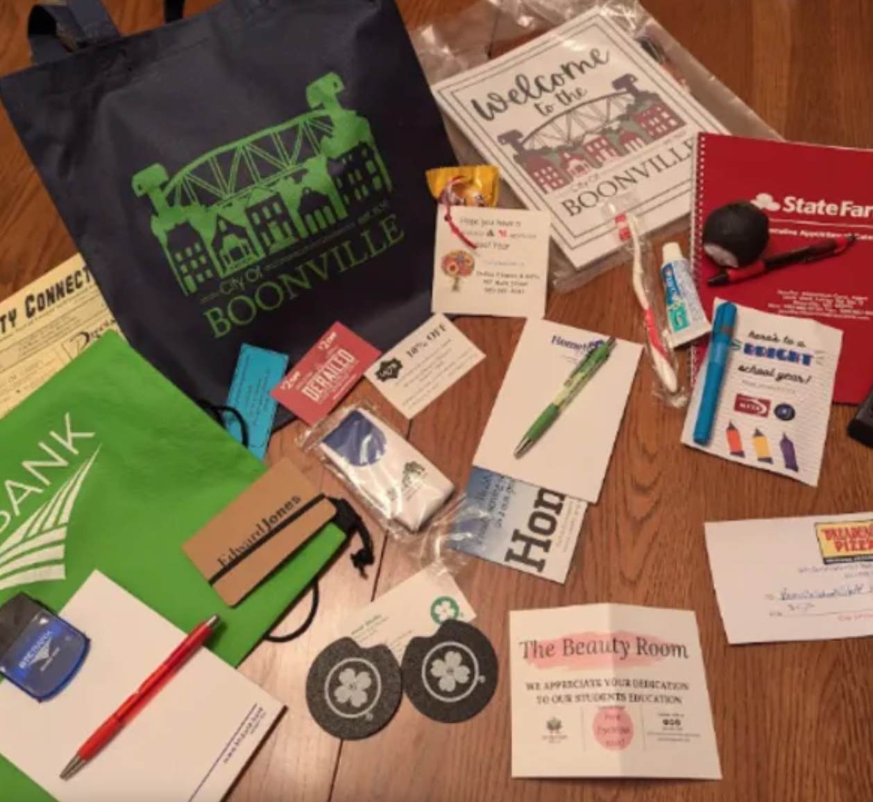 Items are scattered on a table to be put in a welcome bag including coasters, notebooks, pens, a toothbrush, and coupons.