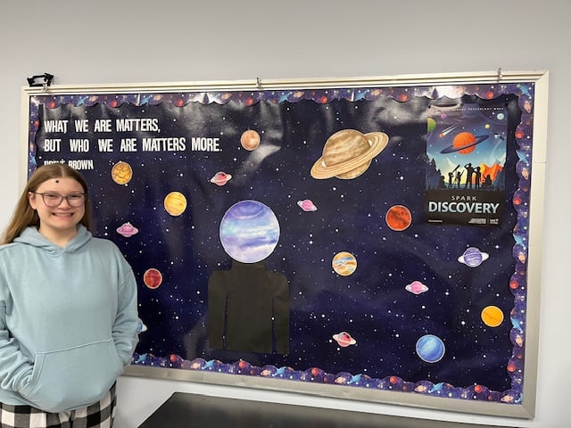 A girl standing beside a bulletin board decorated with space and planet decor