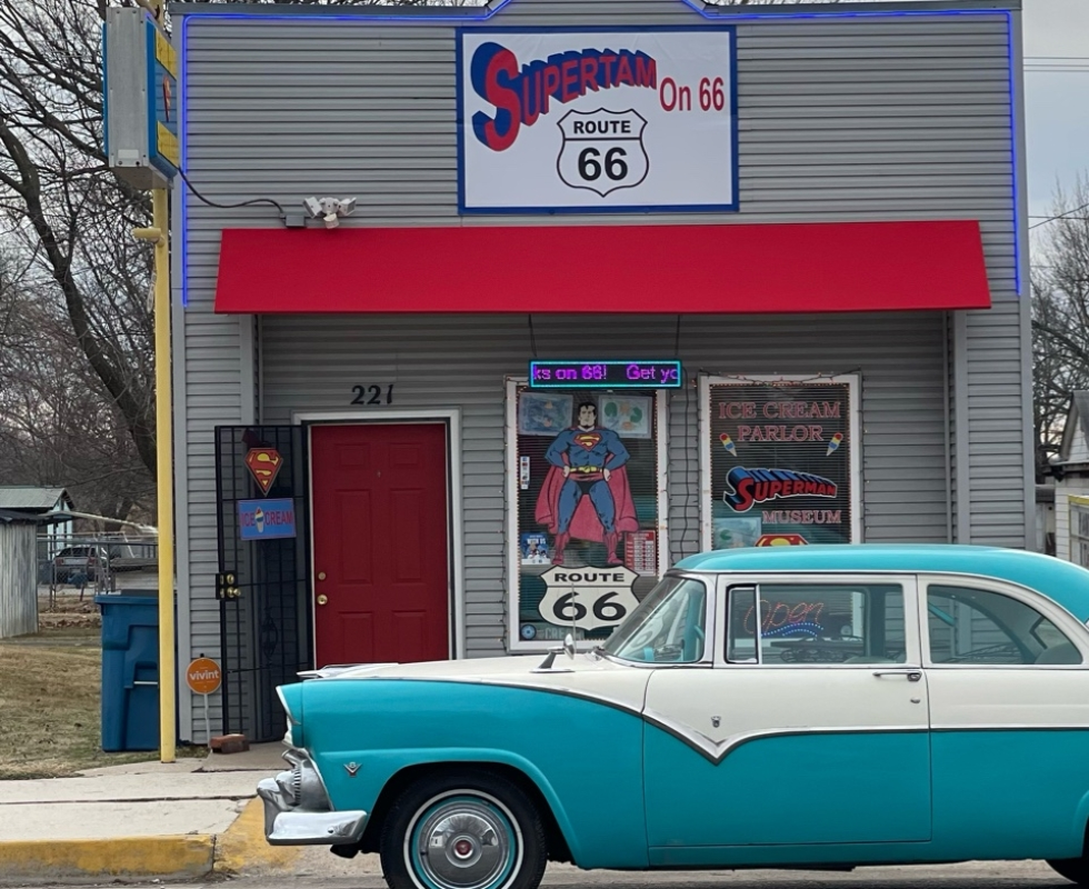 An old-fashioned car outside of a building with a sign that reads "Supertam on 66"