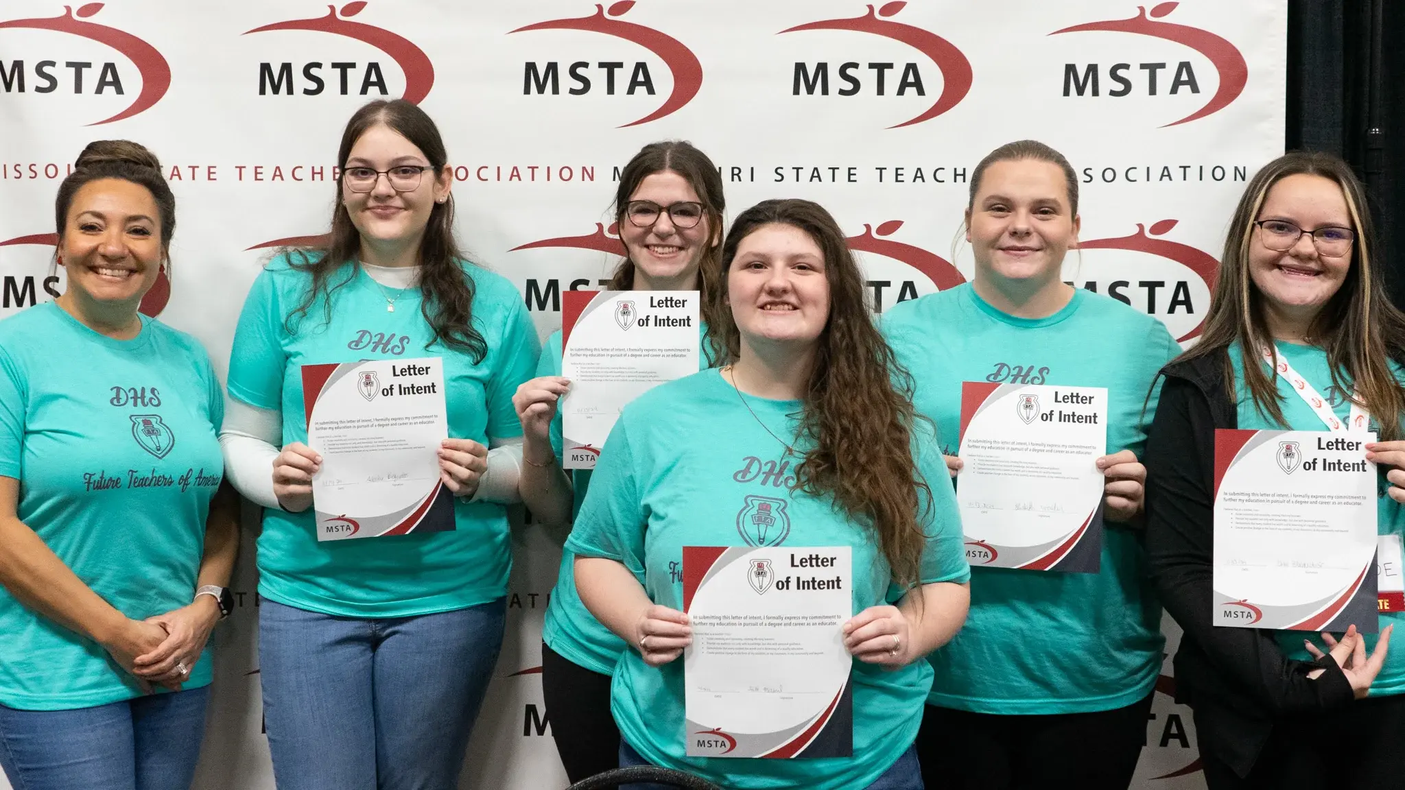 A group of high school FTA students hold signed letters of intent stating they intend to go into the teaching profession