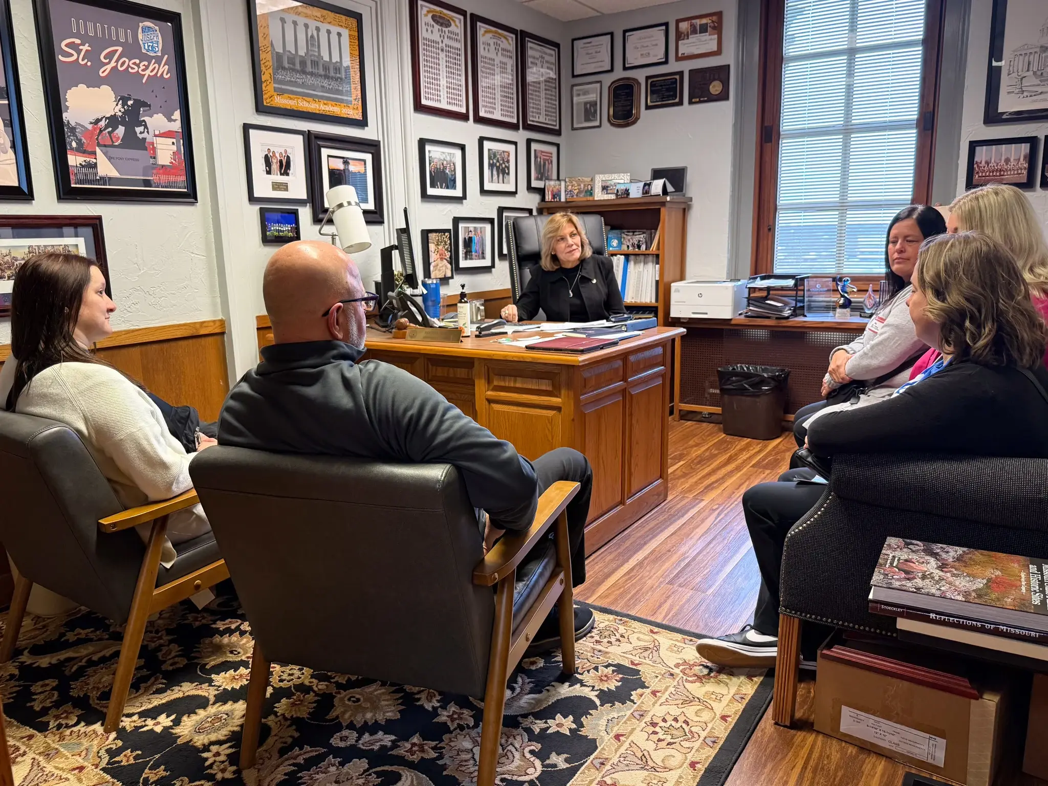 Five St. Joseph MSTA members sit around their state representative Brenda Shields, who sits at a wooden desk