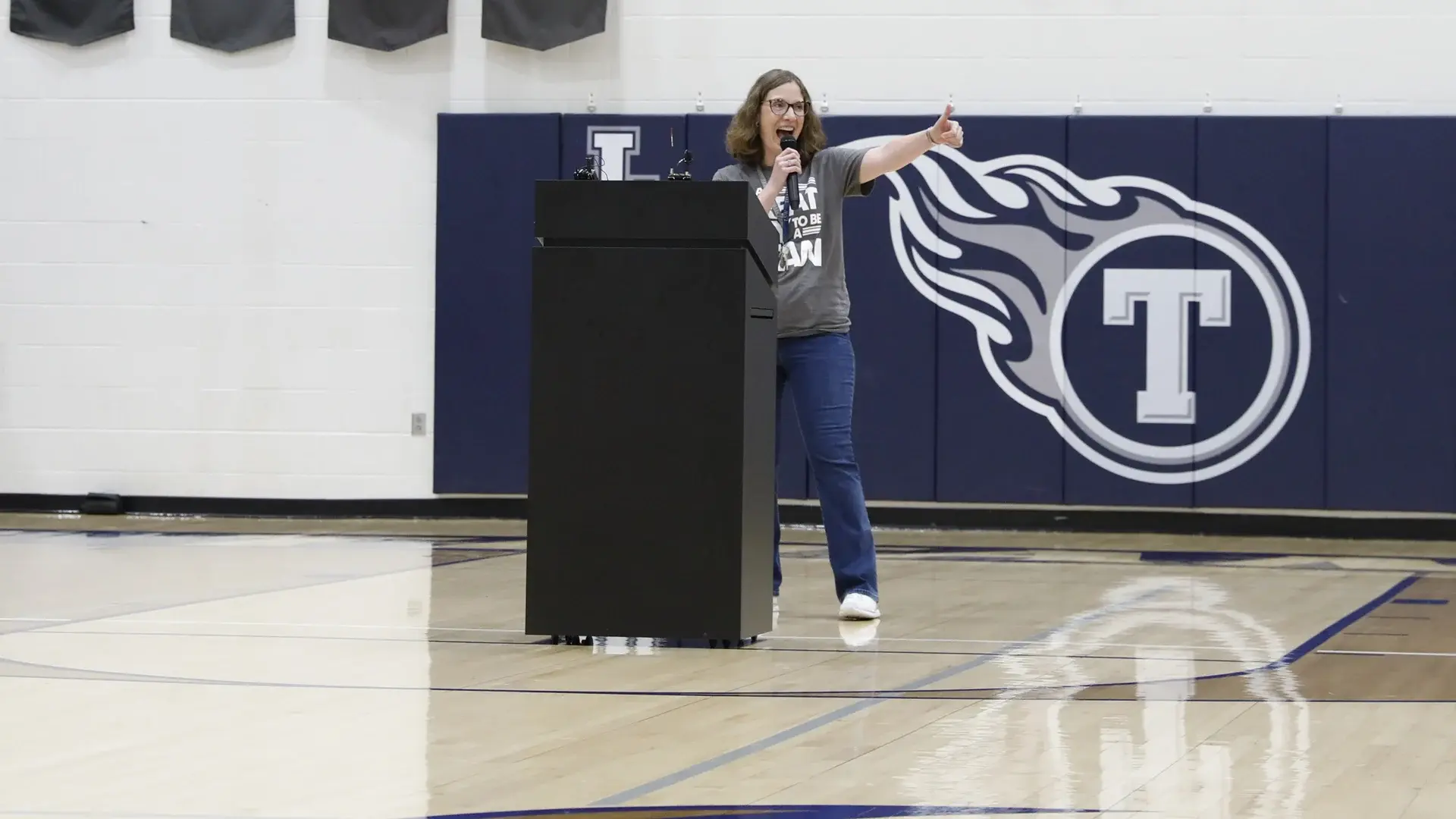 Jennifer Jones speaks from a podium inside a school gymnasium